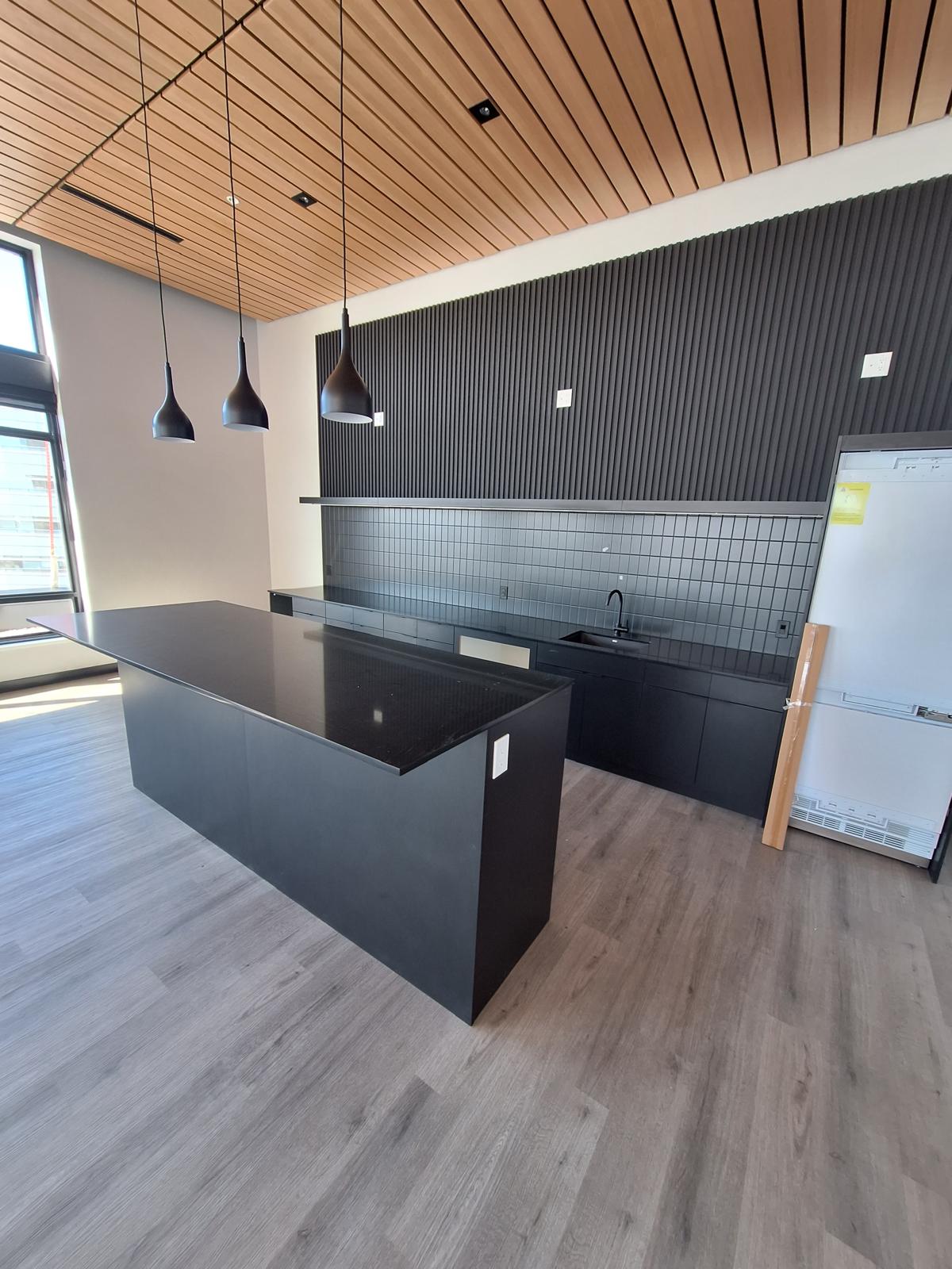 Modern kitchen with a black quartz waterfall island and dark wood slat ceiling